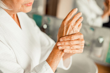 Elderly lady in bathrobe massaging her hands