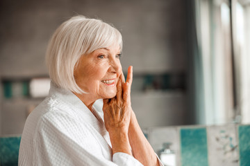 Joyful old lady pressing hands to her cheek