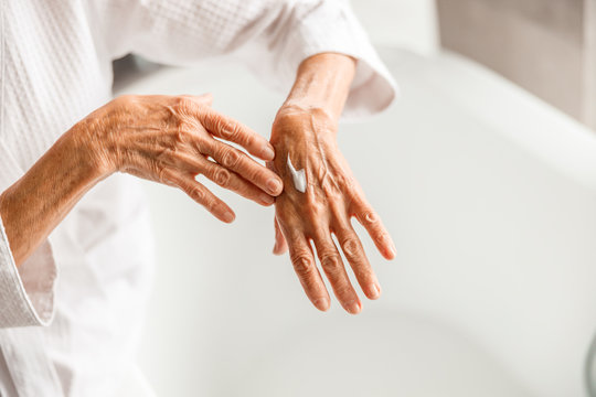 Old woman applying cosmetic cream on hand