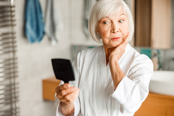 Old woman in bathrobe looking in the mirror