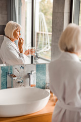 Senior lady in bathrobe taking pills in bathroom