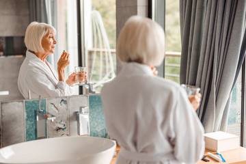 Elderly woman standing by the mirror and taking pills