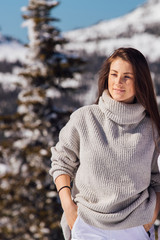 Portrait of a young beautiful brunette woman with blue eyes and freckles on face in winter snowy mountain landscape. Beautiful girl in the winter outdoors.