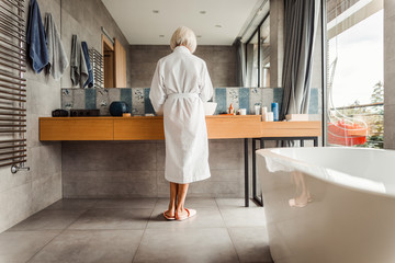 Old woman standing in front of big mirror