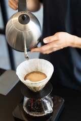 Barista making drip coffee by pouring hot water from goose neck kettle to filter cone