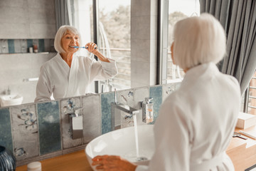 Lovely old lady brushing teeth in bathroom