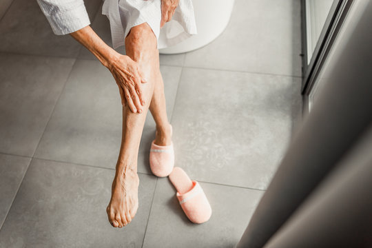 Elderly Woman Sitting On The Edge Of Bathtub And Massaging Leg