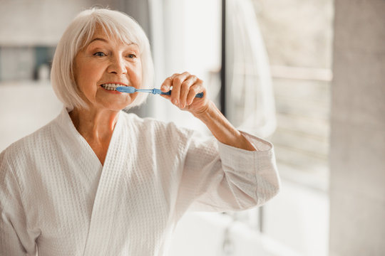Elderly Woman In Bathrobe Brushing Teeth In The Morning