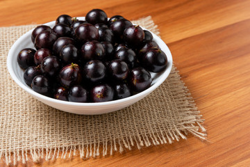 Jabuticaba in the bowl on wooden table. Jaboticaba or Jabuticaba is the native Brazilian grape tree. Species Plinia Cauliflora. Brazilian Berry.