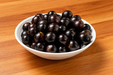 Jabuticaba in the bowl on wooden table. Jaboticaba or Jabuticaba is the native Brazilian grape tree. Species Plinia Cauliflora. Brazilian Berry.