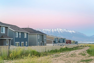 Dirt road along white fences of houses against snow capped mountain at sunset