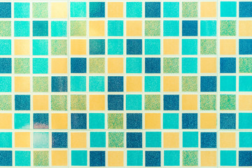 Multiple colored square mosaic tiles texture with white filling decorate the wall in the bathroom.
