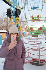 young woman with mobile in hand at amusement park in winter