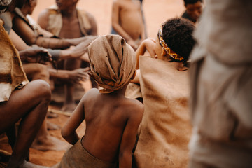 African kid from behind in social group of people sitting in traditional village