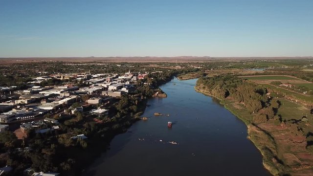 4K summer sunny afternoon aerial drone video: Orange River arched motorway long bridge, grassy islands, boat on the water and busy N10 highway located in town Upington, Northern Cape, South Africa
