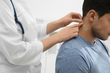 Fototapeta premium Doctor putting sticking plaster onto man's neck indoors, closeup