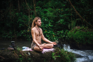 Fototapeta premium Yoga practice and meditation in nature. Man practicing near river