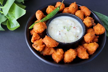 Moong and mix Dal Vada also known as ram laddoo, bhajias or fritters, served with fried chilli, curd & cucumber chutney or raita. Served over dark background. Selective focus. with copy space.