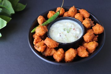 Moong and mix Dal Vada also known as ram laddoo, bhajias or fritters, served with fried chilli, curd & cucumber chutney or raita. Served over dark background. Selective focus. with copy space.