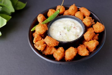 Moong and mix Dal Vada also known as ram laddoo, bhajias or fritters, served with fried chilli, curd & cucumber chutney or raita. Served over dark background. Selective focus. with copy space.