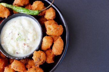 Moong and mix Dal Vada also known as ram laddoo, bhajias or fritters, served with fried chilli, curd & cucumber chutney or raita. Served over dark background. Selective focus. with copy space.
