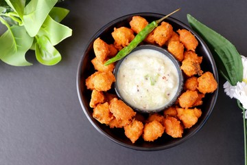 Moong and mix Dal Vada also known as ram laddoo, bhajias or fritters, served with fried chilli, curd & cucumber chutney or raita. Served over dark background. Selective focus. with copy space.