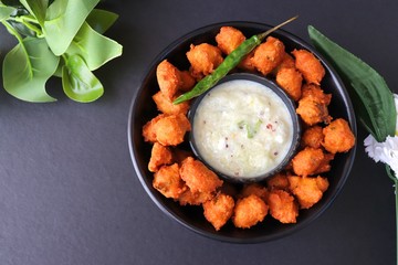Moong and mix Dal Vada also known as ram laddoo, bhajias or fritters, served with fried chilli, curd & cucumber chutney or raita. Served over dark background. Selective focus. with copy space.
