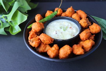 Moong and mix Dal Vada also known as ram laddoo, bhajias or fritters, served with fried chilli, curd & cucumber chutney or raita. Served over dark background. Selective focus. with copy space.