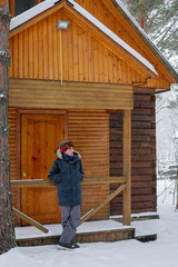 Naklejka na ściany i meble Snowboarding man sitting on snowy porch wooden rustic cottage in the winter woods.