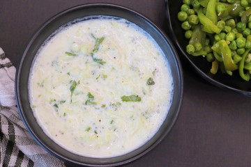Indian Fresh sauce called Raita with herbs, curd and grated cucumber close-up in a bowl on the table. with some saute vegetables like green bell papers and fresh green peas
