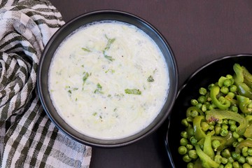 Indian Fresh sauce called Raita with herbs, curd and grated cucumber close-up in a bowl on the table. with some saute vegetables like green bell papers and fresh green peas