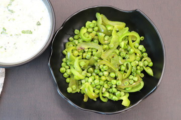 Indian Fresh sauce called Raita with herbs, curd and grated cucumber close-up in a bowl on the table. with some saute vegetables like green bell papers and fresh green peas