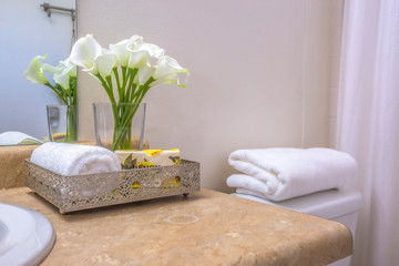 Towels flowers and tissue on teh countertop beside the toilet of a bathroom
