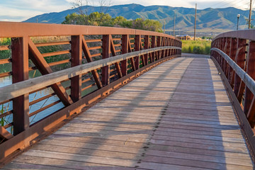 Sunlit wooden deck and metail railing of bridge over lake with mountain view