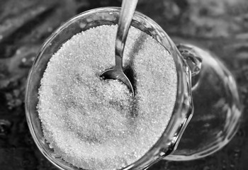 Glass bowl of granulated sugar with spoon on a glass table with a pattern