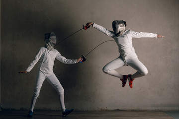 Fencers women with fencing sword. Fencers duel stab attack and jumpconcept.