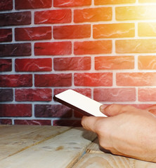 A young man uses a smartphone with a white screen behind a brick wall.