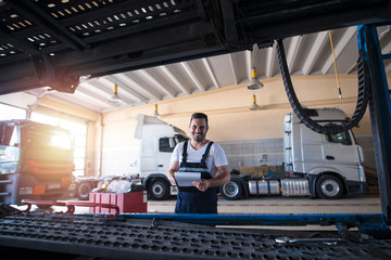 Portrait of smiling mechanic standing in truck repair shop. Vehicle service and truck maintenance.