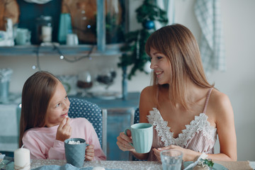Mother with a little daughter sit and have breakfast at table in  kitchen with cup