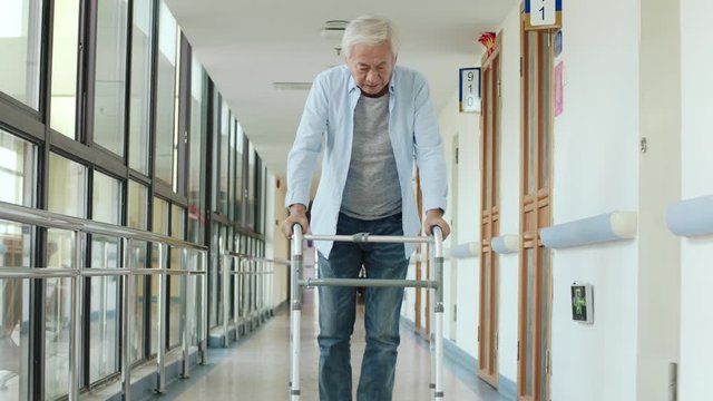asian old man learning to walk using a walker in hallway of nursing home