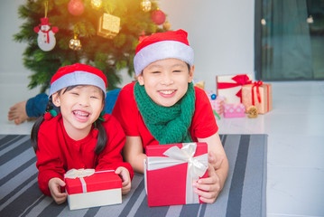 Little asian girl and her brother lying on the floor with gift box and smiling together at home in Christmas holiday.