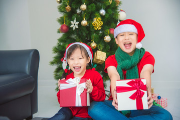 Obraz na płótnie Canvas Little asian girl and her brother sitting on the floor with gift box and smiling together at home in Christmas holiday.