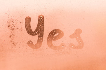 The creative inscription yes on the orange or pink evening or morning window glass with drops 