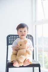 Little asian boy sitting on chair with his teddy bear and smiles.