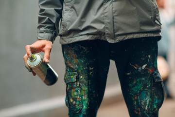 Graffiti artist in clothes stained with paint spray can in hand