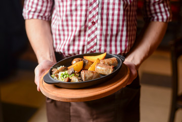 Waiter holds a plate of tasty food. Italian cuisine in restaurant, Baked potato with meat rolls with sauce.