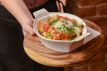 Waiter holds a plate of tasty food. Italian cuisine in restaurant, Pasta with sauce and parmesan cheese and vegetables