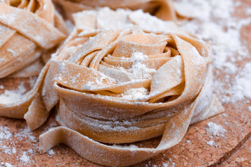 Uncooked fettuccine nest with flour on wooden board Tasty fresh colorful ingredients for cooking pasta. Plaid background