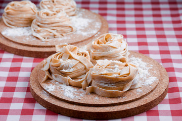 Uncooked fettuccine nest with flour on wooden board Tasty fresh colorful ingredients for cooking pasta. Plaid background