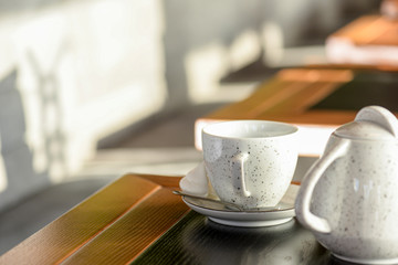 Tea cup with black tea on a small little plate with white tea pot on dark wooden table